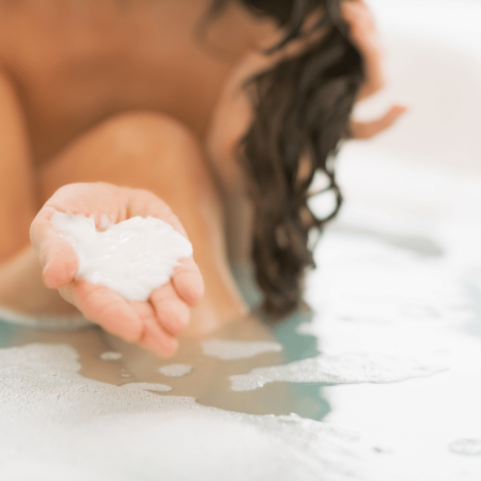 femme avec chevelure bouclée appliquant de l'après shampooing